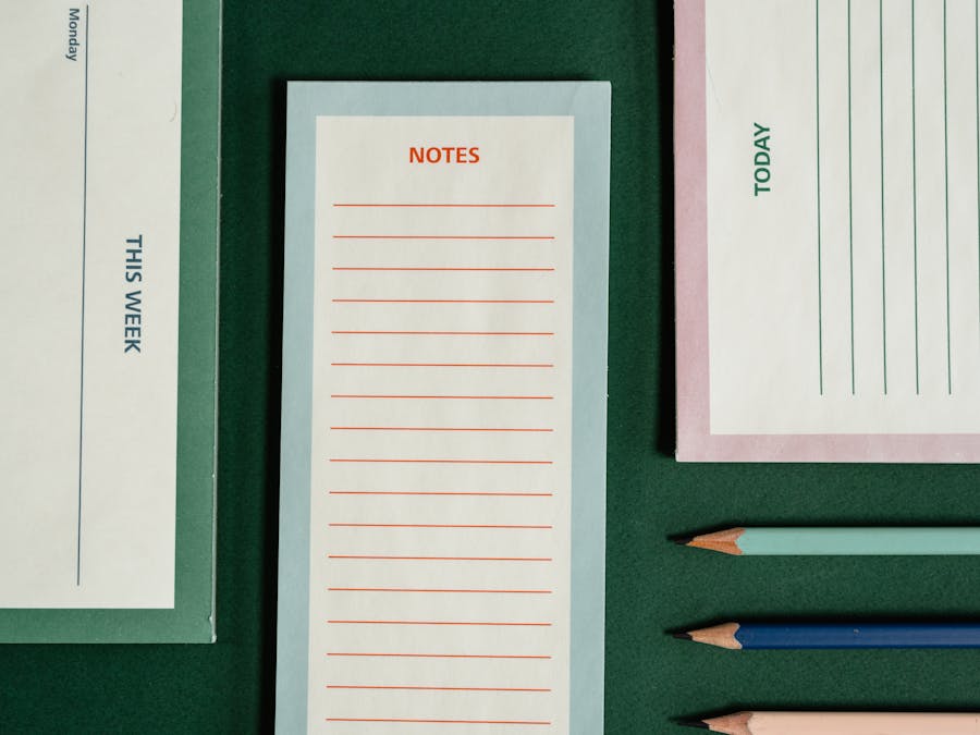 Organized flatlay featuring notepads and colored pencils on a green background.