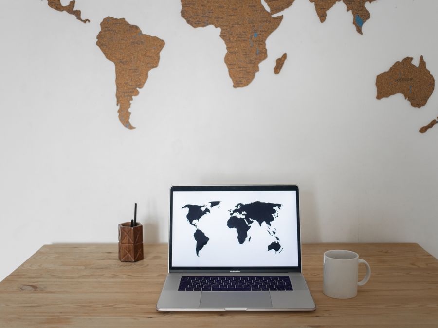 Black world map on laptop screen and ceramic cup with pen container placed on table against silhouettes of continents