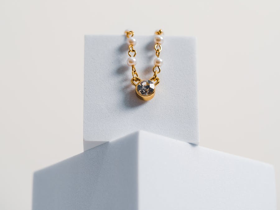 Minimalist photo of a gold necklace with pearls and a gemstone on a white geometric stand.