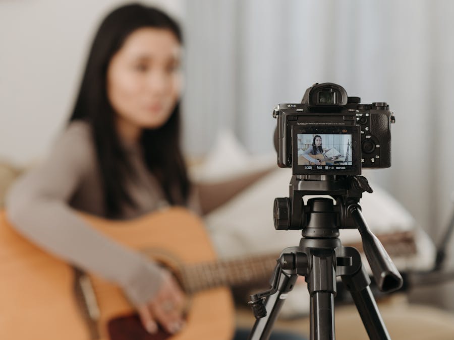 A woman plays guitar while recording a video indoors. Ideal for vlogs or music-related content.