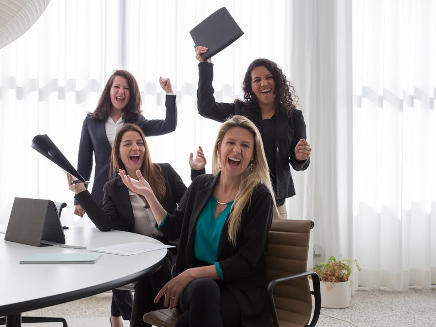 Four women in an office celebrating success and teamwork with enthusiasm.