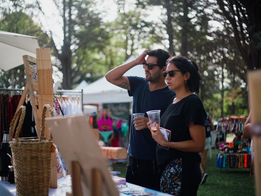 A couple enjoying a sunlit outdoor market, exploring handmade crafts and refreshments.