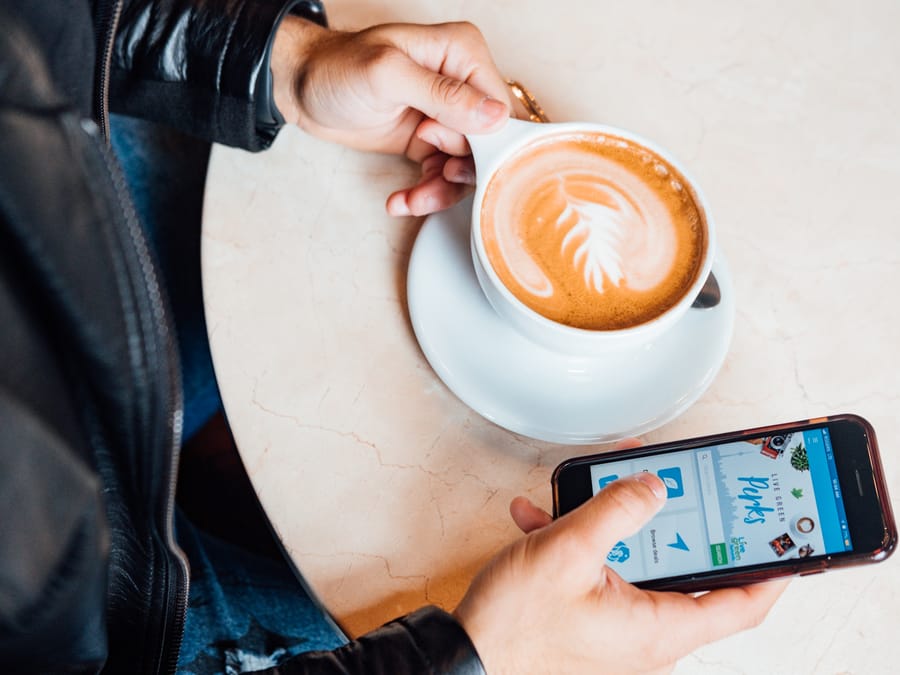 Close-up of person holding latte with beautiful latte art, browsing smartphone.