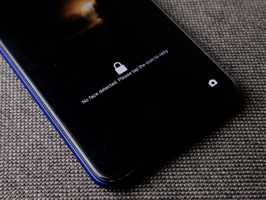 Mobile phone with no face detected message on lock screen on a textured fabric surface.