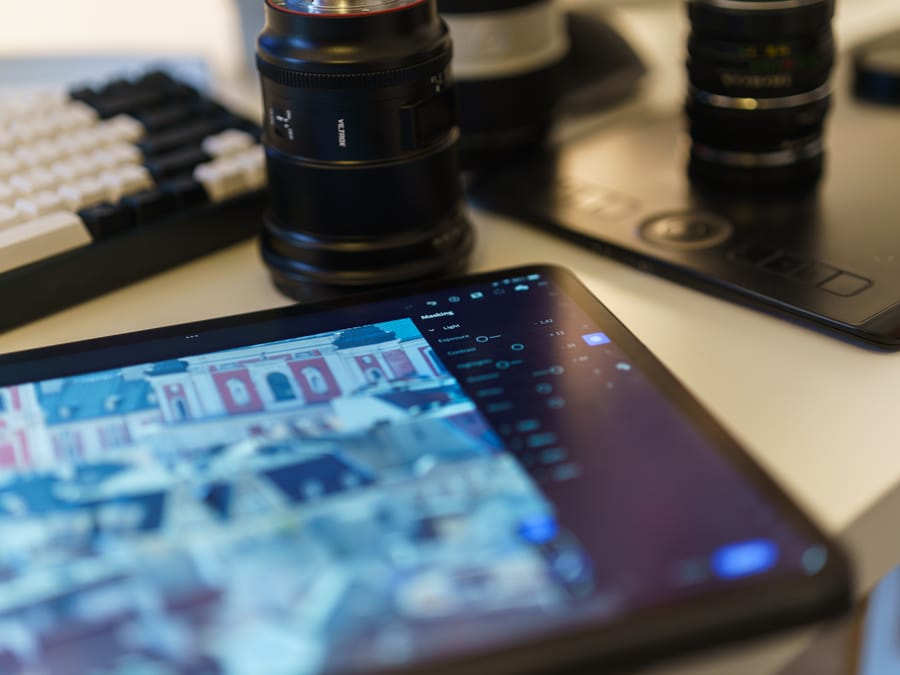 A modern workspace featuring a tablet, camera lenses, and graphic drawing tablet on a desk.