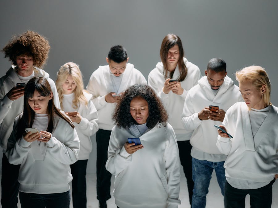 A diverse group of people in white hoodies engaged with smartphones, symbolizing social connection and isolation.
