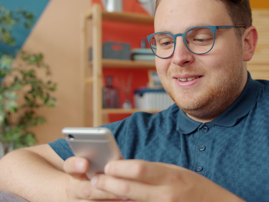 Smiling man wearing glasses and using a smartphone at home.