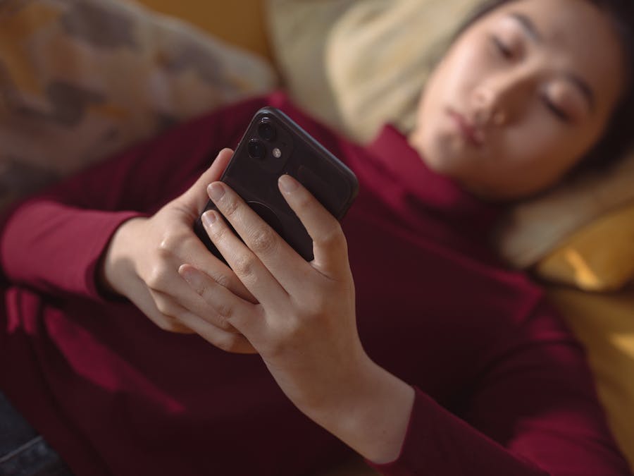 A young woman lying down, holding and using a smartphone for relaxation indoors.