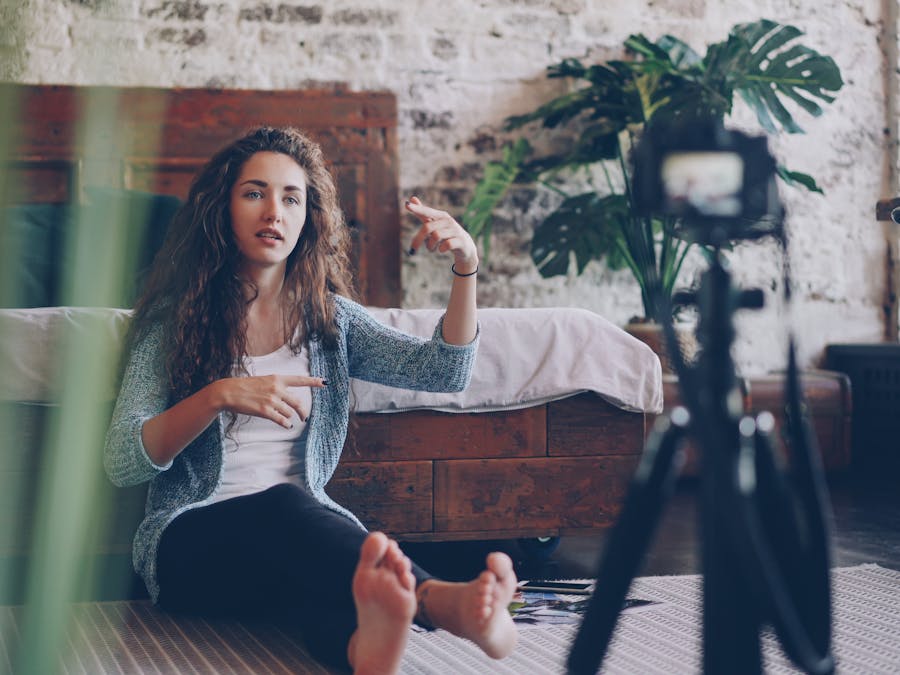 Woman sitting on floor filming vlog, discussing engaging topic. Home setting with cozy atmosphere.