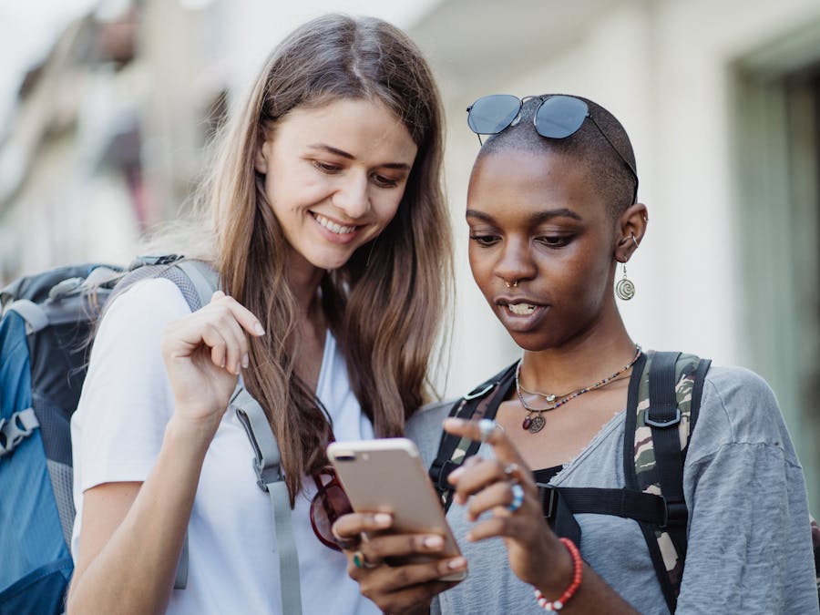 Two friends with backpacks exploring a city, navigating with a smartphone, enjoying a travel experience.