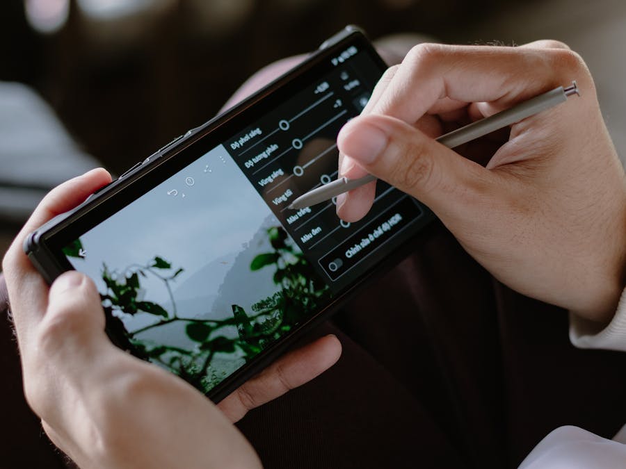 Close-up of a person editing photos on a smartphone with a stylus indoors.