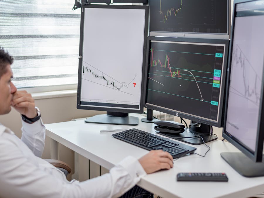 Business professional analyzing financial data on multiple computer monitors at his workspace.