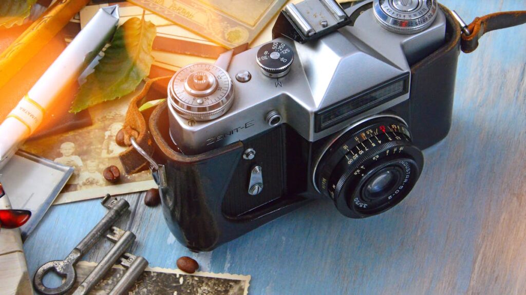 A classic film camera surrounded by nostalgic elements like keys, photos, and roasted coffee beans on a wooden table.