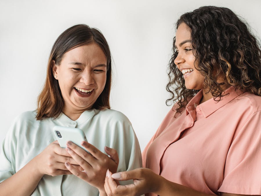 Two diverse women happily looking at and sharing something on a smartphone indoors.