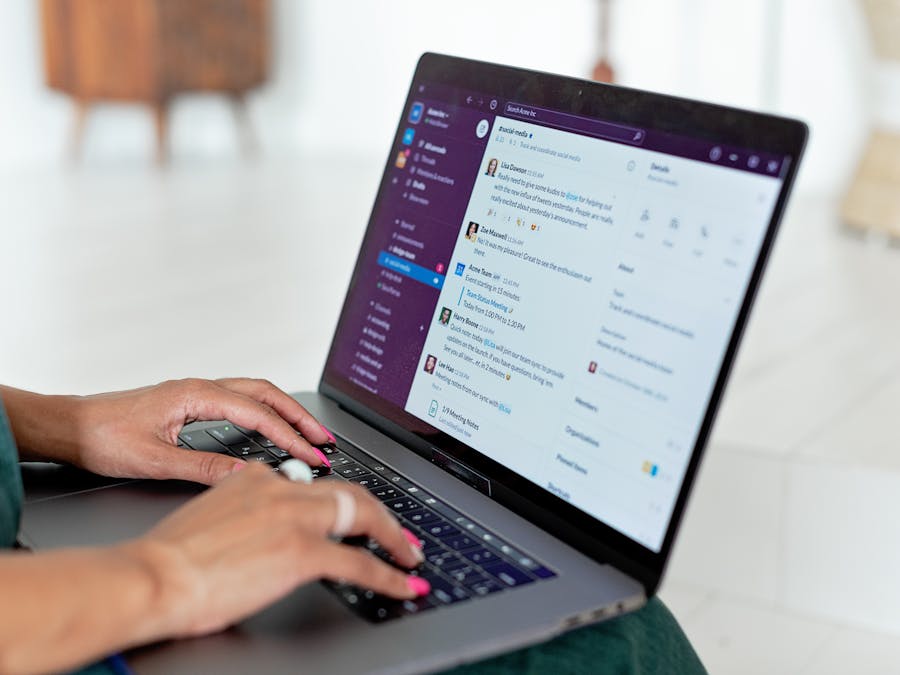 Woman typing on a laptop using a messaging app in a home setting, close-up of hands.