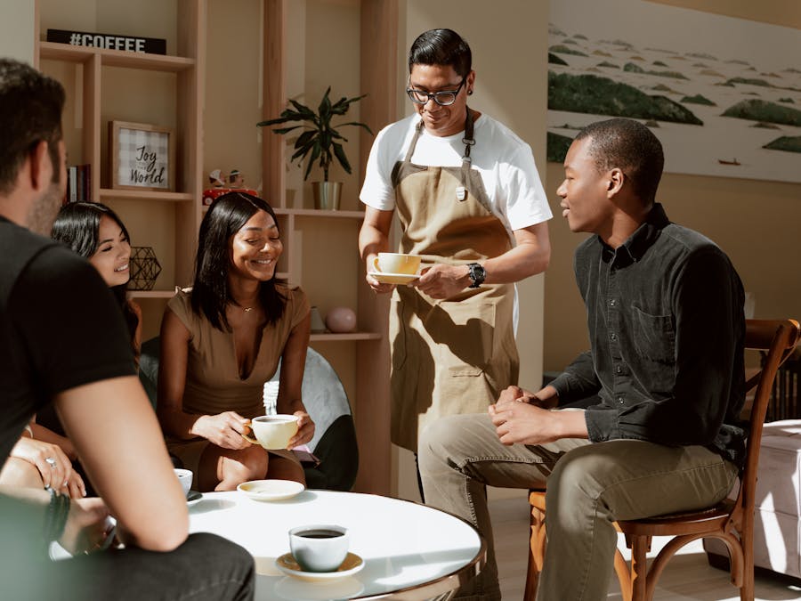 A group of friends enjoying coffee served by a waiter in a cozy café setting.