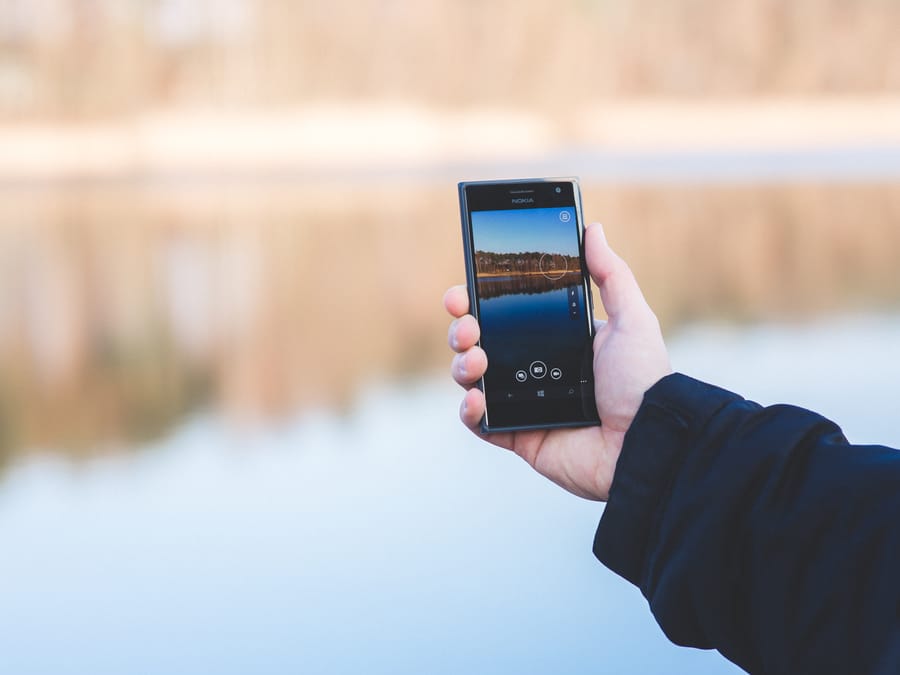 A person taking a photo of a tranquil lake using a smartphone outdoors.