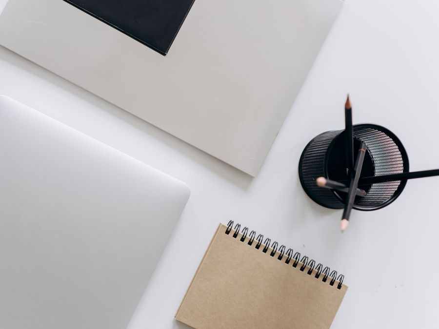 Top view of a minimalist workspace featuring a laptop, notepad, and stationery on a white surface.