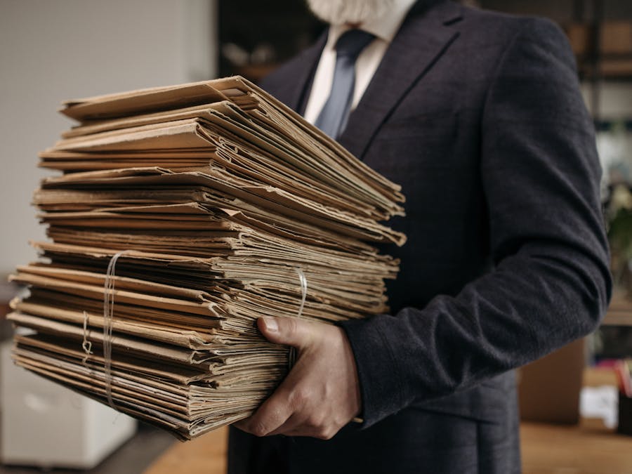 Close-up of business professional holding a large stack of brown folders in an office setting.