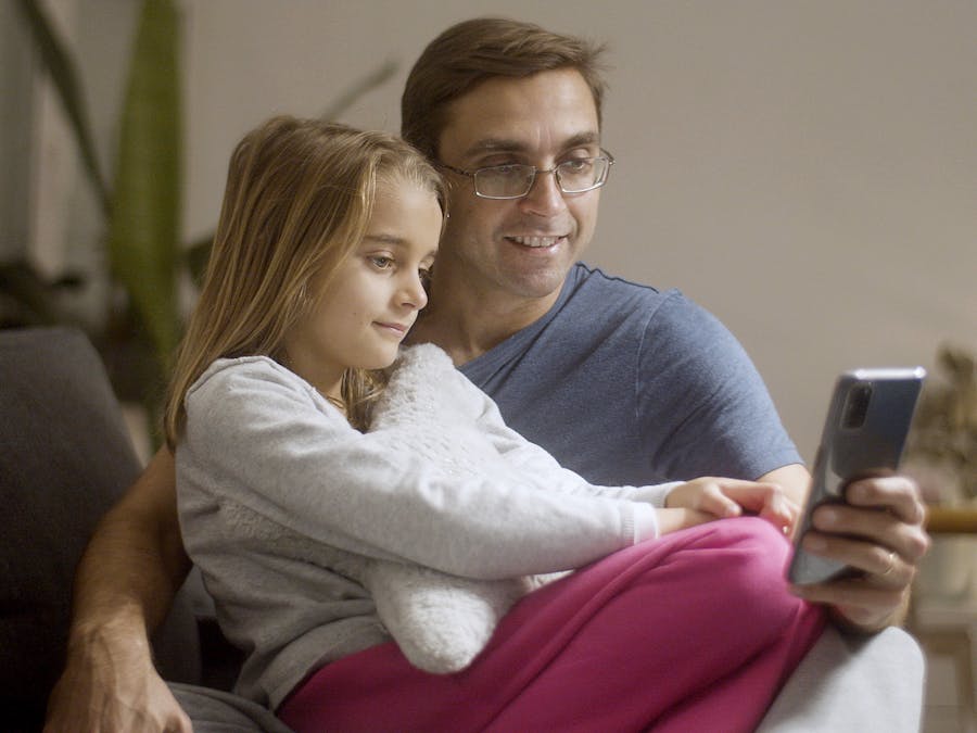 A father and daughter enjoying a relaxed moment together using a smartphone indoors.