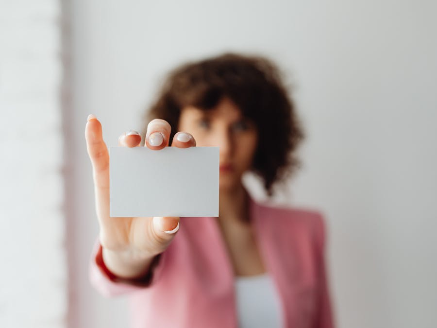 A professional woman in pink suit presenting a blank business card indoors.