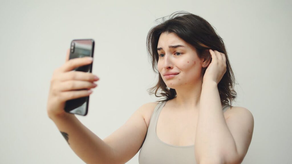 A young woman in a tank top taking a selfie with a worried expression on her face.