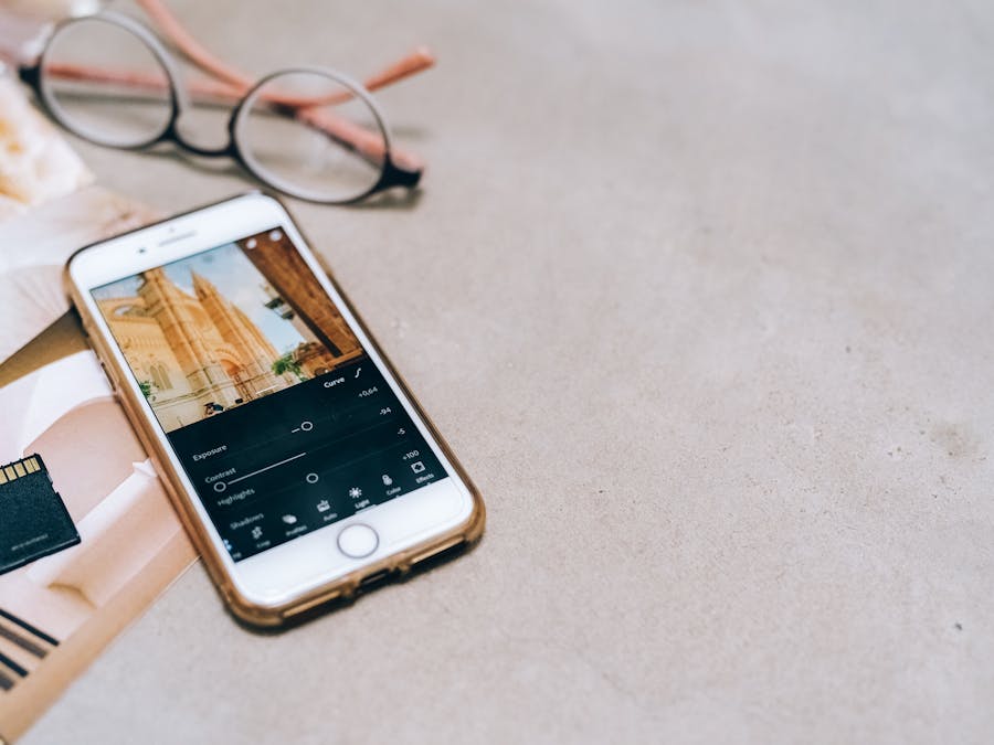 Smartphone displaying a photo editing app, next to a memory card and glasses on a table.