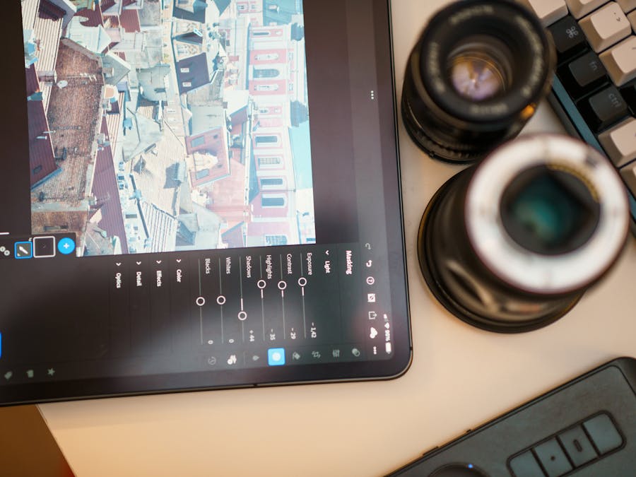 A modern workspace featuring a tablet editing cityscape photo, camera lens, and keyboard.