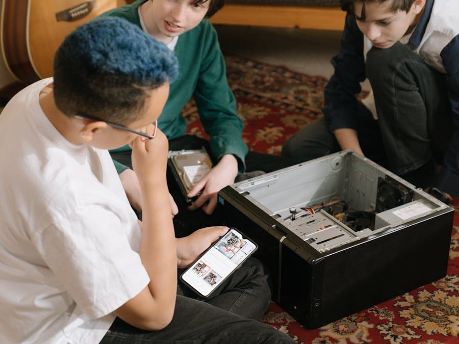 Three young boys repairing a computer indoors, focused and learning teamwork skills.