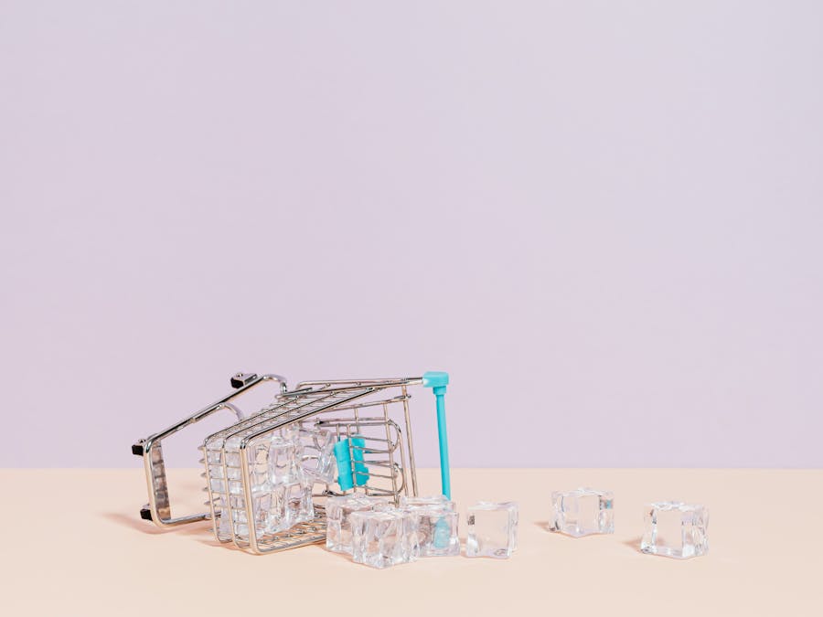 Tipped shopping cart with ice cubes on pastel background, offering creative copy space.