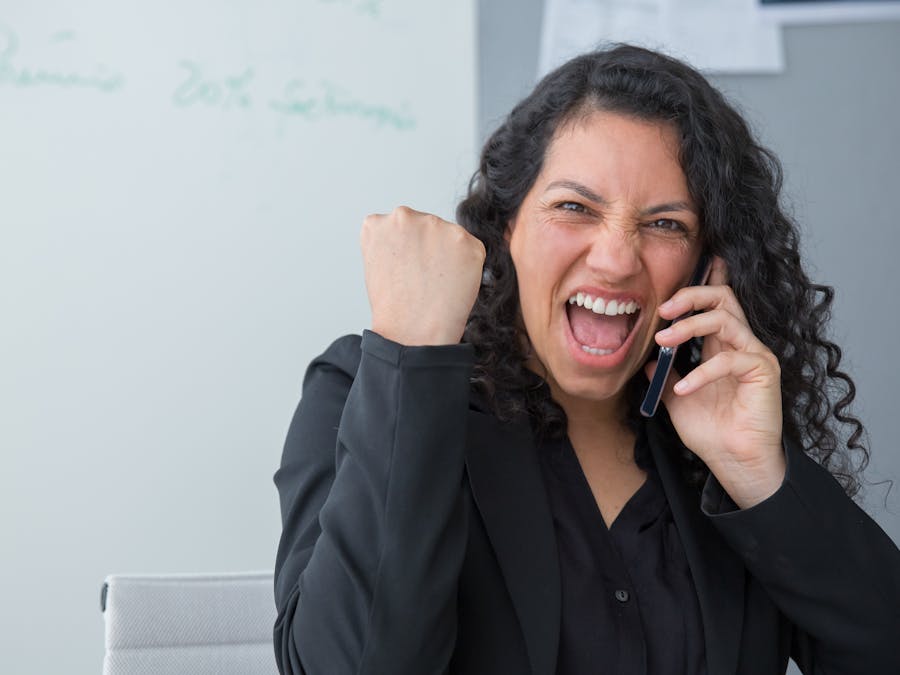A joyful businesswoman with curly hair celebrates success while talking on the phone indoors.