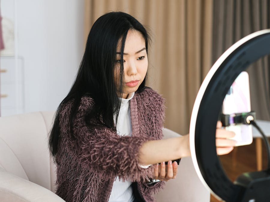 An Asian woman vlogs at home using a smartphone and ring light, perfect setup for influencers.