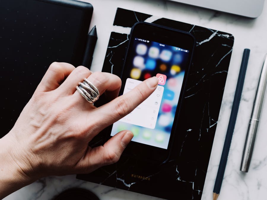Top view of anonymous person using smartphone app tapping on screen while working with digital devices and pen and pencil placed on white marble table at home