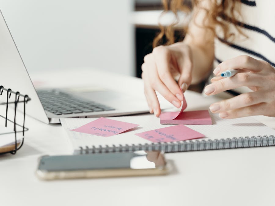 Woman organizing notes with a laptop and smartphone at a modern workplace.