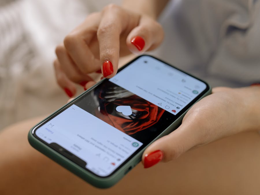 Close-up of a woman with red nails using a smartphone indoors, showcasing social media browsing.