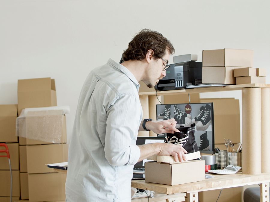 A businessman working in an online store packing shoes in a cardboard box.