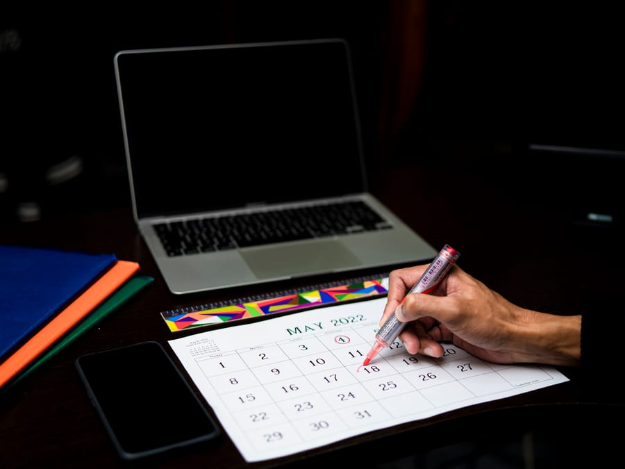 A person plans on a calendar at a desk with a laptop and phone, May 2022.