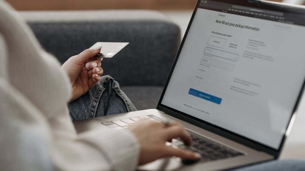Woman holding credit card shopping online on a laptop from a couch.