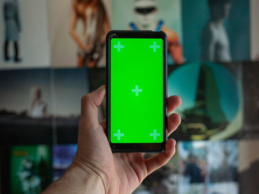 A close-up of a person's hand holding a smartphone with a green screen for editing on a background of blurred images.