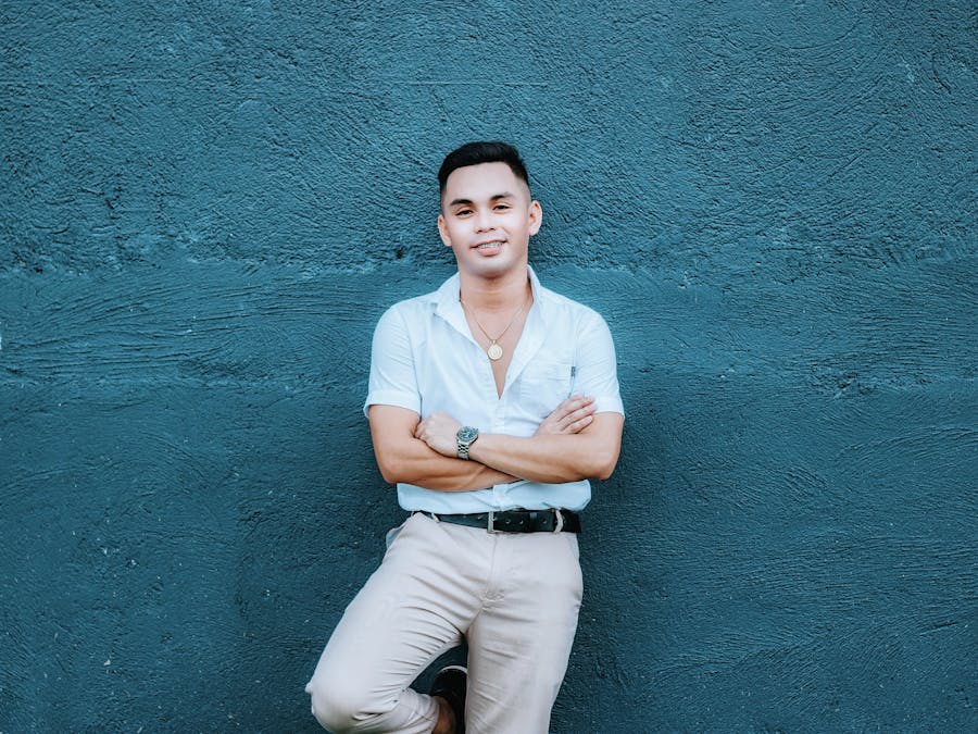 Smiling man in casual attire posing confidently against a blue wall.