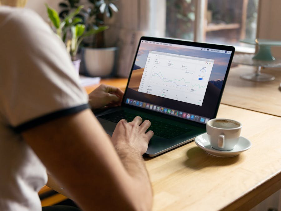 Person working on a laptop with analytics in a cozy home office setting, coffee in hand.