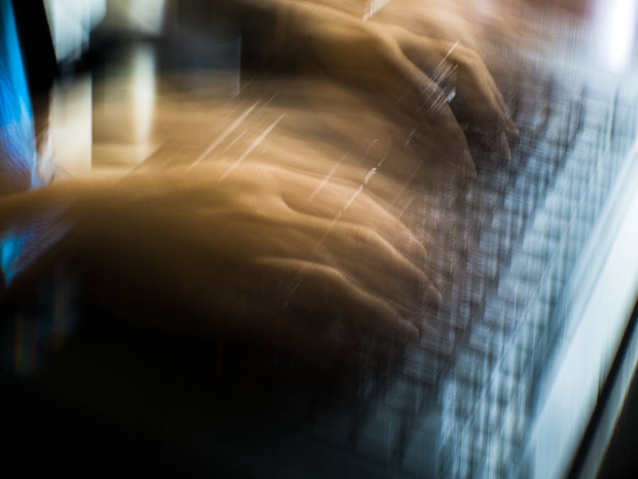 From above of crop anonymous person typing on keyboard of laptop in long exposure