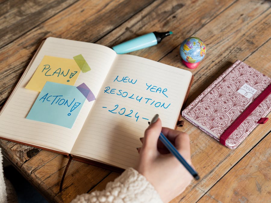 Person writing New Year 2024 resolutions in a notebook with sticky notes for planning and action.