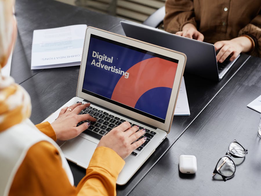 Two professionals work on laptops focusing on digital advertising in an office setting.