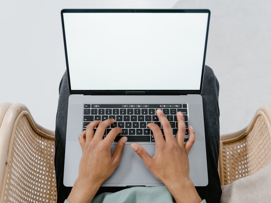A person typing on a laptop with a blank screen, viewed from above in a casual setting.