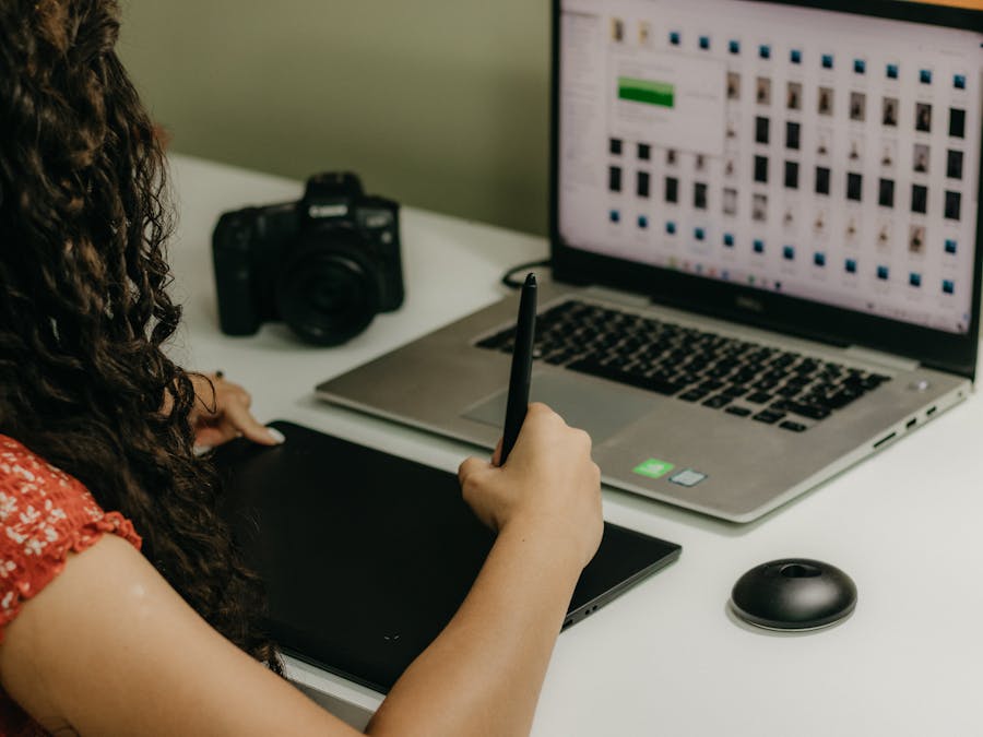 Woman using pen tablet with laptop and camera in creative workspace.