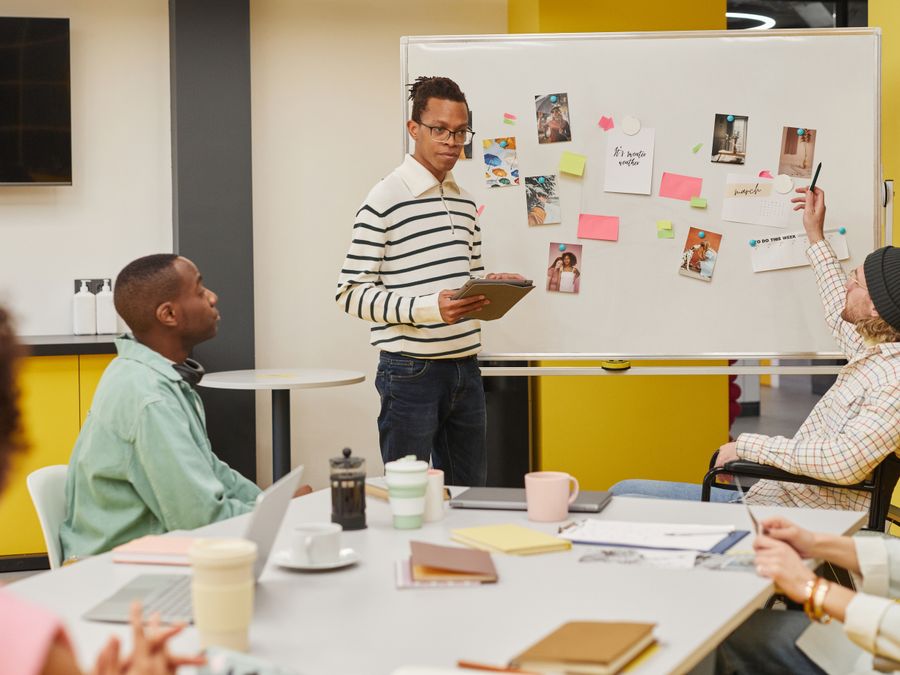 A diverse team engaged in a collaborative meeting around a whiteboard in a modern office setting.