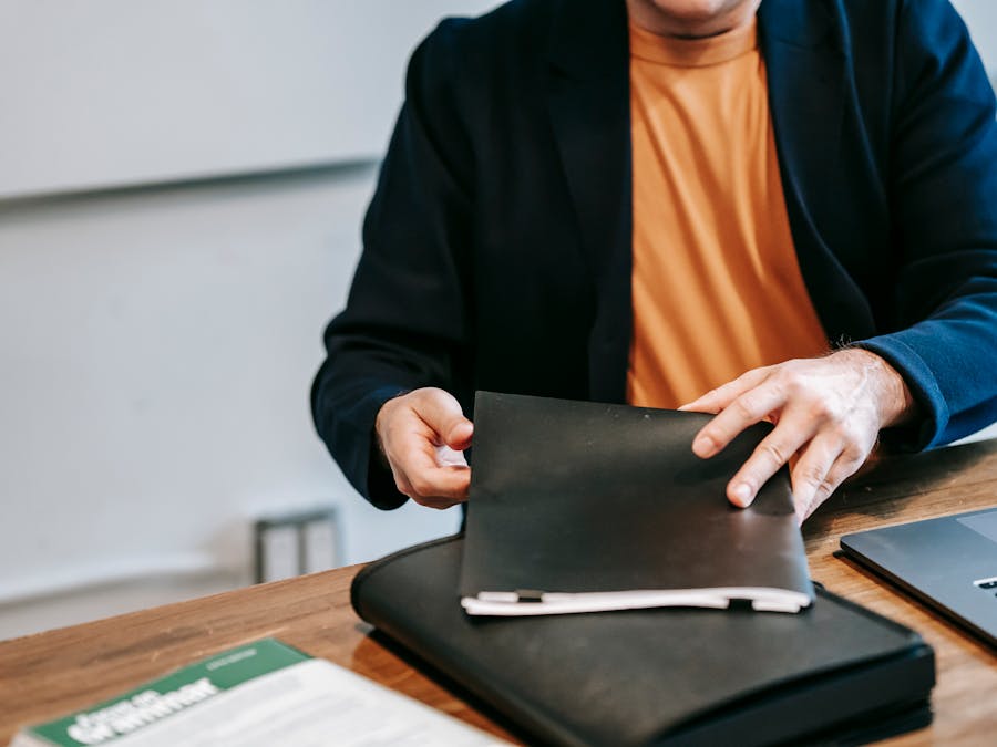 A business professional in a blazer organizing documents at a wooden desk inside an office.
