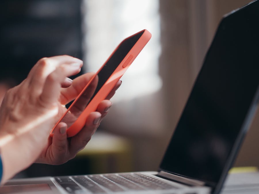 Adult using a smartphone and laptop indoors, showcasing modern technology and multitasking.