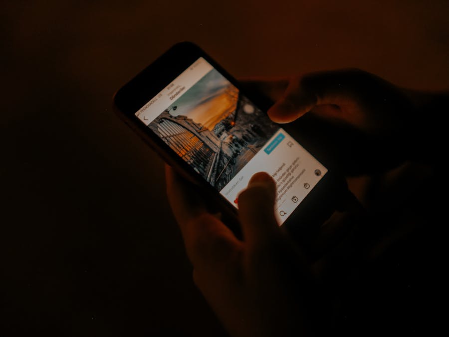 Hands holding a smartphone browsing social media in low light.